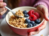 Frische Beeren mit Joghurt und knusprigen Flocken in einer bunten Frühstücksschale serviert