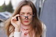 © st.kolesnikov - Portrait of a young woman squinting and holding glasses while trying to see clearly, representing poor vision, blurred eyesight, or difficulty focusing in everyday life.