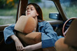 © SHOTPRIME STUDIO - Young woman with long hair resting in a vintage car, exuding a contemplative mood, wearing a denim jacket, surrounded by a natural green background.