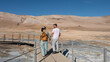 © Fokke Baarssen - Two tourists walk hand in hand along the boardwalk at Hverir, a geothermal area in Iceland. The striking, barren land and blue skies create a breathtaking backdrop for their adventure.