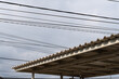 © yusrmuttaqien - A modern corrugated PVC silent rain roof structure under a complex network of tangled electrical power lines against a cloudy sky.