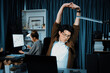 © InfiniteFlow - Sales manager working on desk with stretching body with arm ache at over late night time at modern home office with secretary sitting back investing dynamic stock market on project database. Infobahn.