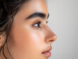 Close-up profile view of a beautiful woman's face with thick eyebrows on a gray background.