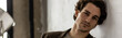 © ArtSys - Banner. Young sexy handsome fit man in a brown suit looking at the camera sitting on a chair in the studio. Grey background, loft interior, studio. Causal stylish men's clothes, watch
