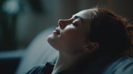 Wall Mural - Cinematic close up of a young woman lying down with her head tilted back, eyes closed, and a peaceful expression, conveying a sense of deep relaxation and serenity in a dimly lit indoor setting