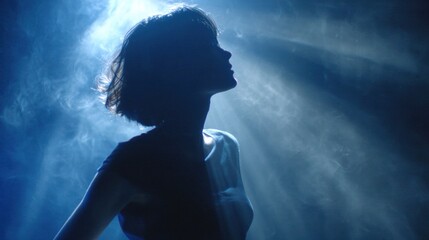Poster - Silhouette of a young woman with short hair striking a pose under vibrant blue stage lights, surrounded by swirling atmospheric smoke, evoking a dramatic and artistic mood