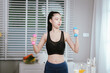 © Natthawadee - A focused young woman in a sports bra is exercising with light dumbbells, dedicated to her home fitness routine.
