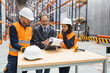 © Koldo_Studio - Manager showing documents to warehouse workers standing at table wearing safety vests and helmets