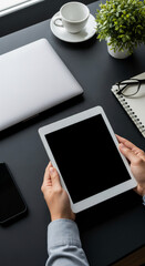 Aufkleber - Overhead view of hands holding tablet with blank screen, laptop, notebook, and coffee cup on dark desk, showcasing modern workspace mockup ideal for advertisement