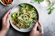© The Picture Pantry - A person holding a bowl of zucchini noodles with pesto, bacon, and parmesan cheese, with a fork ready to eat.