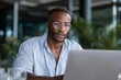 © Milos - A focused young man with glasses works on a laptop in a bright space surrounded by greenery, showcasing the connection between technology and nature in a modern work environment.