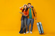© Home-stock - Ready for vacation. Couple holding map, man standing with suitcase, wearing travel neck pillow and backpack, showing their readiness for holiday adventure, yellow background