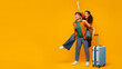 © Home-stock - Excited European couple having fun, standing with suitcase on orange background, panorama with free space for design, banner