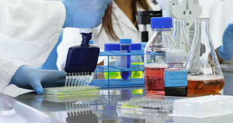Poster - Pipetting gloved hands transferring solution into 96-well microplate at lab bench with tube rack