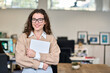 © insta_photos - Happy businesswoman, female company worker intern or corporate manager holding laptop. Young smiling professional business woman standing in modern office working, looking at camera. Portrait