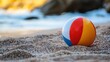 © Mey - A colorful beach ball on a sandy beach with rocks in the background.