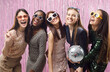 © Studio Romantic - Portrait of a young happy group of women friends in dress clothes and funny sunglasses having fun and looking at camera on studio pink foil background. Party and celebration concept.