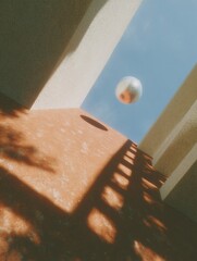 Aufkleber - Abstract architectural scene with metallic sphere floating above terracotta surface and textured walls under blue sky, showcasing modern minimalism and light play