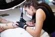 © YuliaSmyt - Close-up of a tattoo artist creating a floral tattoo on a woman's hand using a tattoo machine in studio