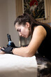 © YuliaSmyt - Close-up of a tattoo artist creating a floral tattoo on a woman's hand using a tattoo machine in studio.