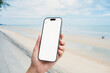 © Nuttima - Hand holding a smartphone with a blank screen, on the sea and sandy beach background. Summer vacation concept.
