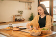 © saltdium - A Cheerful Asian woman making a fresh meal on a wooden counter, Homemade Sandwich Preparation
