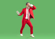 © Studio Romantic - Full length shot of carefree happy showman or show presenter dressed in elegant red suit, striped tie and shades, dancing and moving actively, isolated over green studio background