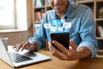smiling man receives messages and emails on his smartphone while working at home