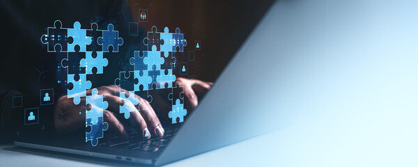 Poster - Hands typing on laptop with digital puzzle pieces representing teamwork and global collaboration for business success on gradient blue background.