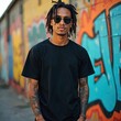 © Pete - Young man with dreadlocks in sunglasses stands against graffiti art. Tattooed arms, blank black t-shirt mock up. Urban street style, casual wear, youth culture. Front view, model poses outdoors in