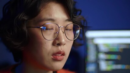 Poster - Close Up Of Young Asian Woman With Code Reflecting In Glasses Against A Dark Blue Background And Visible Computer Screen
