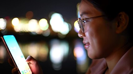 Poster - Woman With Glasses Uses Smartphone at Night With Bokeh City Light Reflections In Water