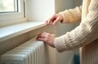 © Pete - Woman touches cold radiator, wearing warm knitted sweater in room. Concept of energy crisis, no heating, rising prices. Home temperature, cold winter season, central heating problems.