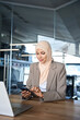 © Stock 4 You - Middle Eastern muslim businesswoman manager ceo using cell phone mobile application. Smiling young indian woman in hijab holding smartphone sitting in office working online at desk on gadget. Vertical