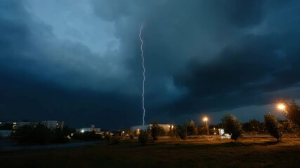 Aufkleber - Lightning strikes the ground near a city park on a summer evening. Dark clouds hang overhead and street lamps illuminate the scene.