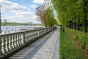 Poster - Scenic Riverside Walkway With Lush Greenery and Clear Sky in a City Park During a Sunny Afternoon