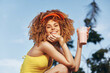 © SHOTPRIME STUDIO - Young woman enjoying a smoothie outdoors in a bright yellow outfit and a visor, with a cheerful smile against a blue sky and green foliage