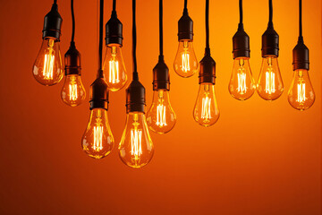 Poster - Hanging Edison light bulbs glowing with warm illumination on orange background.