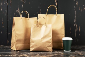Poster - Brown paper bags and coffee cup on wooden surface against dark rustic background.
