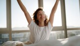 Woman stretching in her bed with joyful and relaxed expression, enjoying bright morning in modern room with large windows and natural sunlight. scene exudes happiness and freshness