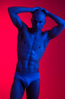 © SHOTPRIME STUDIO - Athletic man posing under vibrant blue and red lights, embracing a striking artistic style that emphasizes body form and strength in a captivating visual presentation.