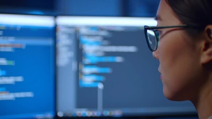 Focused software developer reviewing code on multiple monitors intensely analyzing
