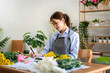 © Katcha - Female florist in apron writing details of order in notebook on the table while creating and making flower