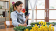 © Katcha - Female florist in apron reading details of order in smartphone and writing information in notebook while