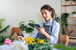 © Katcha - Female florist in apron reading details of order in smartphone and writing information in notebook while