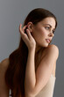 © SHOTPRIME STUDIO - young woman with long brown hair posing gracefully against gray background wearing beige top with natural light highlighting her calm and thoughtful expression