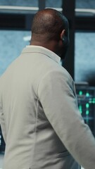 Poster - Vertical video Employee walking in high tech data center with hardware used to host websites. IT professional overseeing dimly lit server farm setup helps companies stay connected, camera B