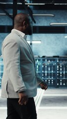 Poster - Vertical video Employee walking in high tech data center with hardware used to host websites. IT professional overseeing dimly lit server farm setup helps companies stay connected, camera A
