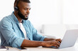 © Prostock-studio - Black millennial man in headset working remotely with laptop at home office, young african american freelancer guy using computer, typing on keyboard while sitting at desk near window, copy space