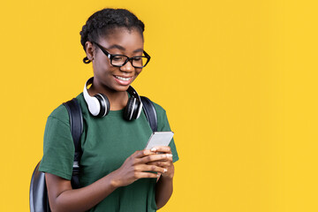 Aufkleber - Happy African Female Student Using Smartphone Networking And Texting Online Standing Over Yellow Background. Young Woman Using Mobile Application On Phone. Studio Shot